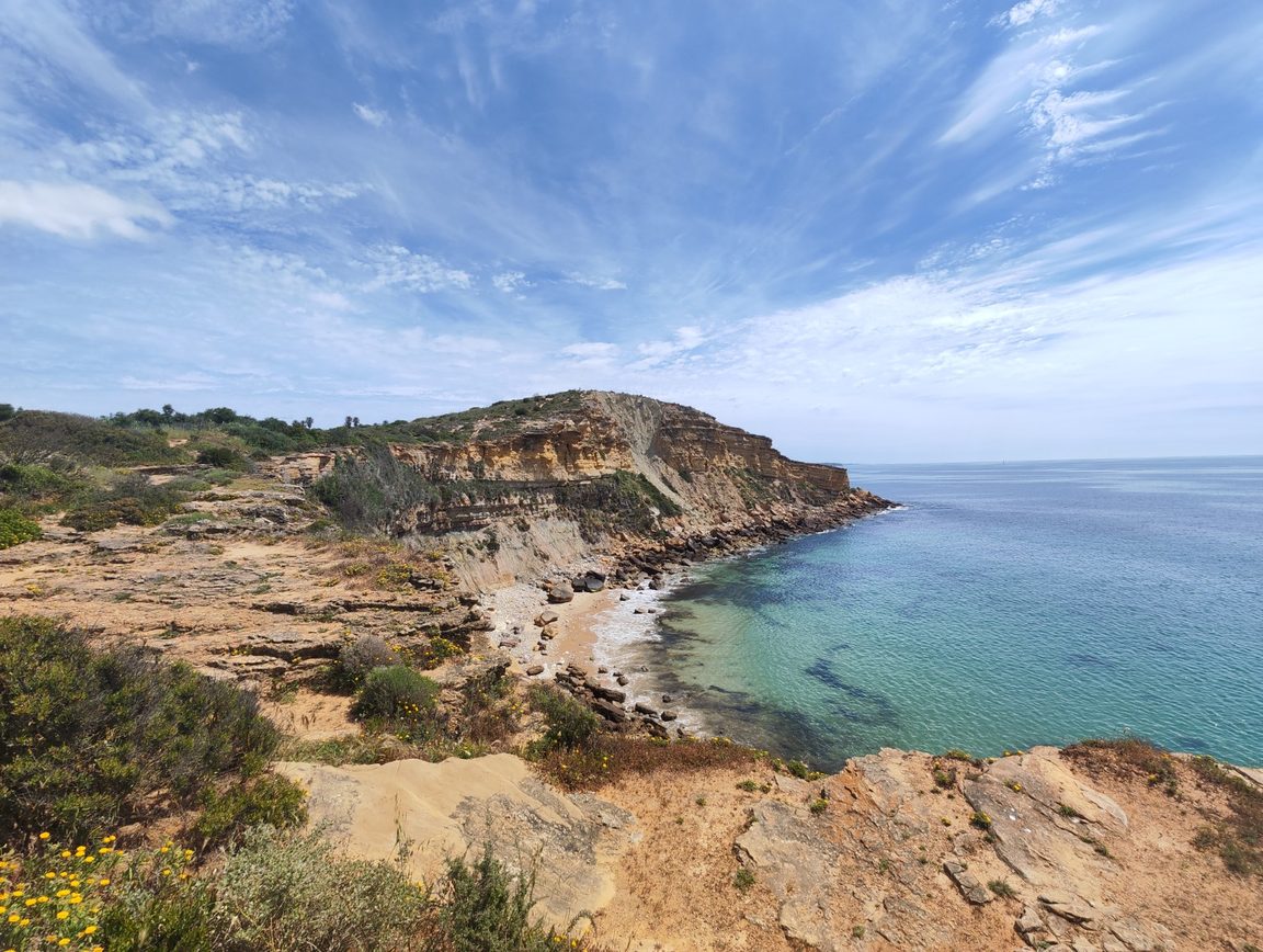 A sandstone headland on the Atlantic coast, a small beach in the bay below and open sea to the horizon.
